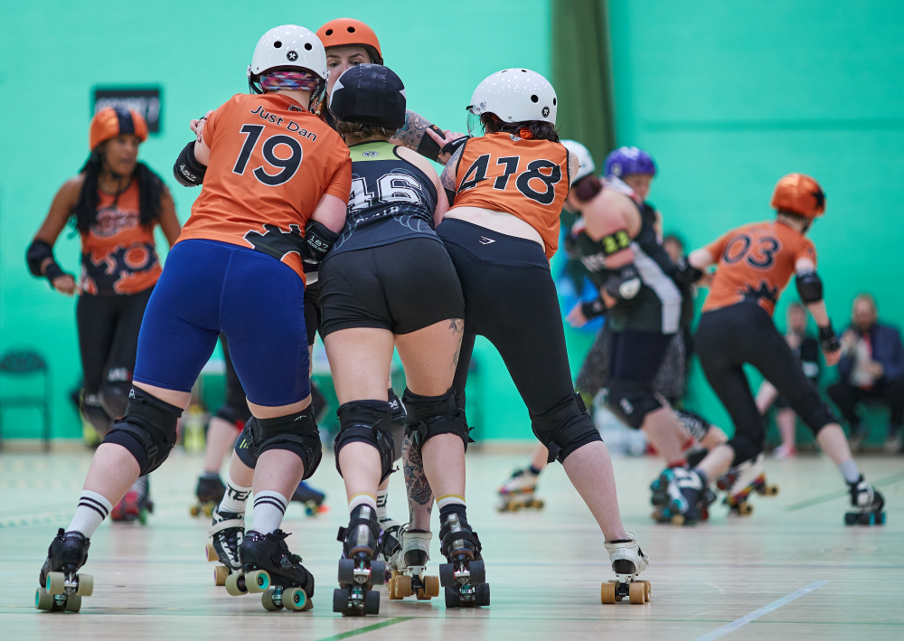 Two SSRD skaters - JUst Dan and Gemma, form a flat two wall as an opposing tries to break through the middle. The brace, Ron, is holding the two SSRD skaters together