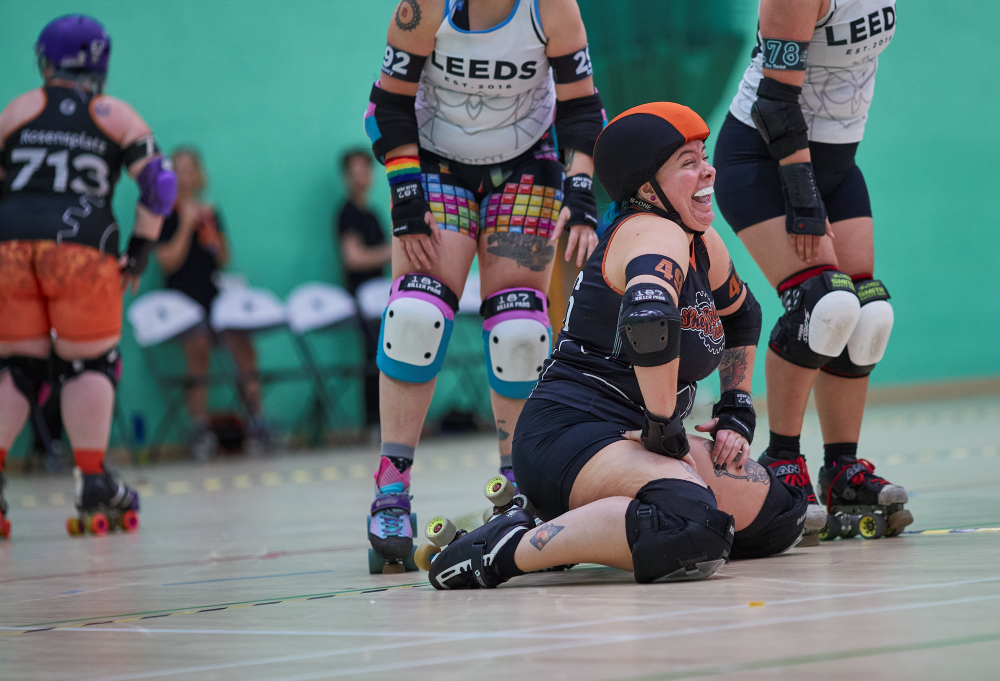 Our skater Cherry, is kneeling on the floor smiling and laughing - likely after being hit down by the opposing team